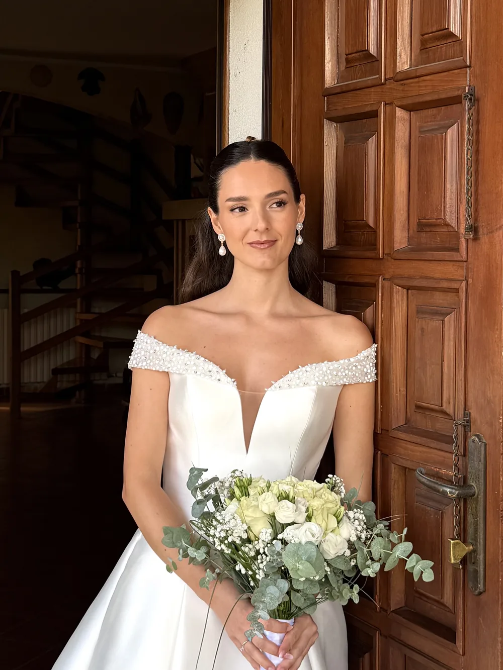 Sposa sul portone con bouquet di rose bianche ed eucalipto